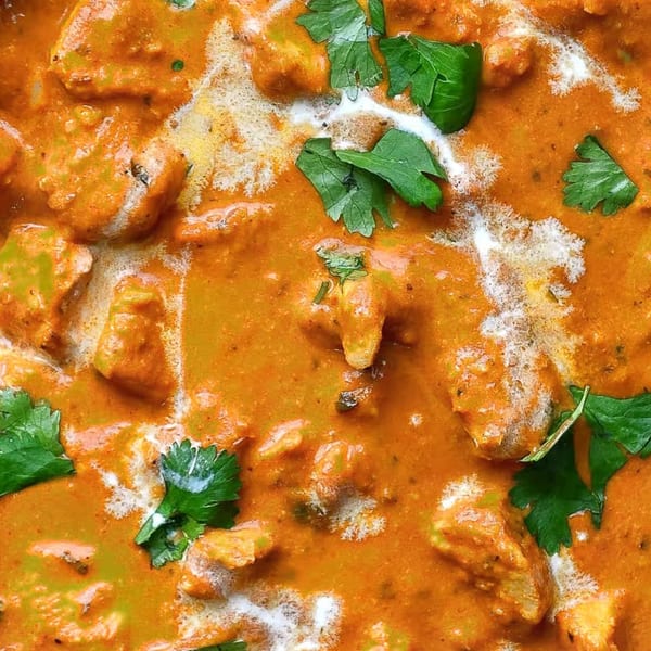 Close-up of Indian butter chicken curry with white cream swirls and fresh green cilantro.