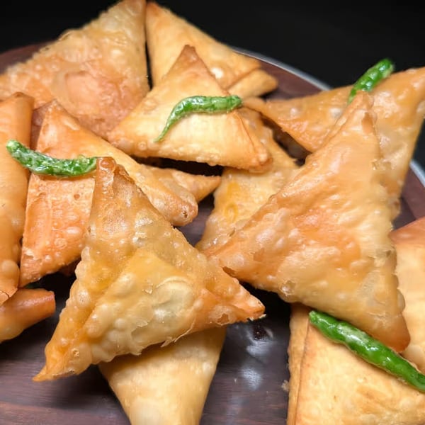 A close-up of golden-fried Indian samosas, garnished with vibrant green chilies on a dark surface.
