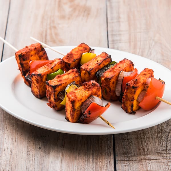 Sweet Magic Indo-Chinese Restaurant's paneer tikka skewers with bell peppers and onions on a white plate.